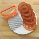 Fourchette à Légumes Ergonomique en Acier Inoxydable et Plastique dans une assiette blanche avec des tomates coupées en tranche sur une table en bois